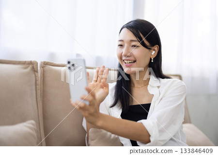 A woman holding a smartphone and waving with a smile A woman holding a smartphone and waving with a smile 133846409