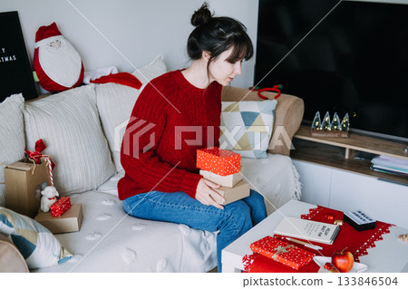 Person sits on sofa holding stack of wrapped gifts over coffee table displaying HOLIDAY BUDGET PLAN on notebook. Budget-friendly Christmas, holiday financial planning, money management, saving tips. Person sits on sofa holding stack of wrapped gifts over coffee table displaying HOLIDAY BUDGET PLAN on notebook. Budget-friendly Christmas, holiday financial planning, money management, saving tips. 133846504