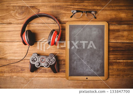Flat design flat-lay showing headphones, game controller, chalkboard and eyeglasses on wooden table Flat design flat-lay showing headphones, game controller, chalkboard and eyeglasses on wooden table 133847700