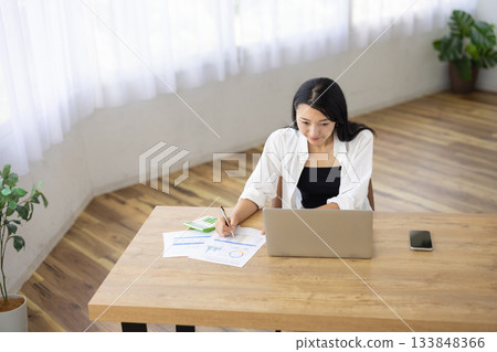 一名女子一邊用筆記型電腦工作一邊做筆記 133848366