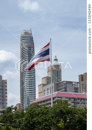 Thai flag waving in front of modern skyscrapers in Bangkok showcasing urban architecture 133848494