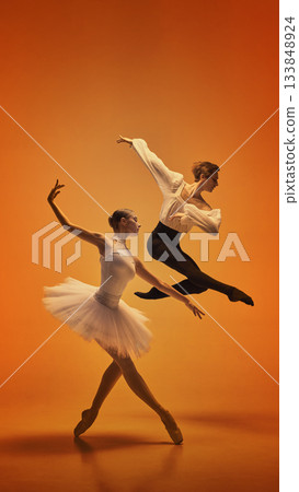 Ballet dancers captured in dramatic jump and poised stance on vivid orange background 133848924