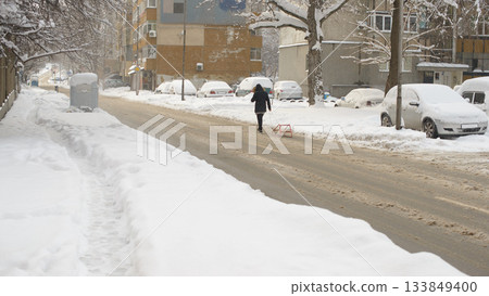 Snowy Urban Street With Person Walking and Pulling Sled Snowy Urban Street With Person Walking and Pulling Sled 133849400