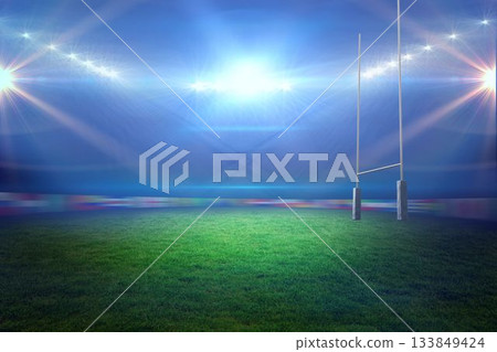 Rugby goalposts with padded bases are standing on floodlit turf at night, floodlights are glowing 133849424