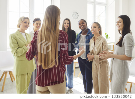 Group of women standing in bright office, listening to their colleague, engaging in discussion. Group of women standing in bright office, listening to their colleague, engaging in discussion. 133850042