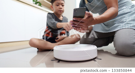 Father and son engaging with smart home device. Controlling robot vacuum with smartphone. Father and son engaging with smart home device. Controlling robot vacuum with smartphone. 133850844