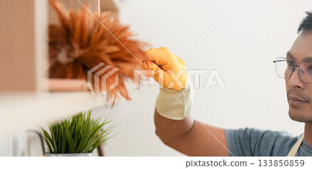 Home Cleaning. Man dusting shelves with yellow gloves. 133850859
