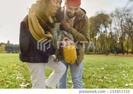Parents lifting laughing child in autumn park, playful family moment outdoors 133851335