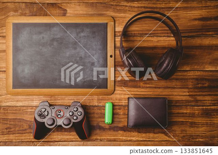 Showing flat top-down scene with wooden chalkboard, headphones, controller, green USB drive, wallet Showing flat top-down scene with wooden chalkboard, headphones, controller, green USB drive, wallet 133851645