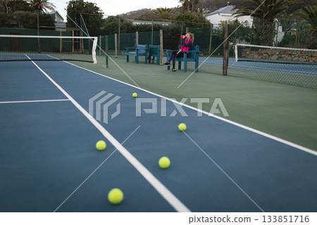 Child holding water bottle is sitting on blue bench by tennis court in flat design 133851716