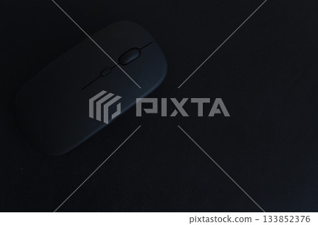 A black computer mouse sits on a dark surface A black computer mouse sits on a dark surface 133852376