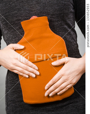 Girl having stomach ache, holding hot water bottle 133852933