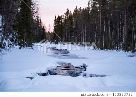 winter river flowing through snowy forest landscape in lapland 133853782