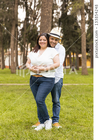 A man and woman are standing in a grassy field, smiling at the camera A man and woman are standing in a grassy field, smiling at the camera 133854248