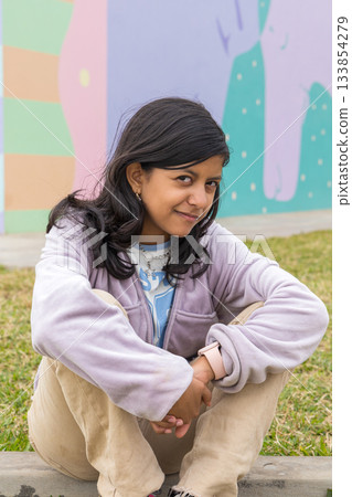 A young girl is sitting on the grass with her hands on her knees A young girl is sitting on the grass with her hands on her knees 133854279