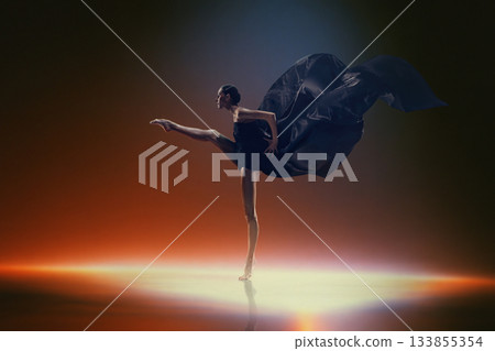Ballet dancer in extended leg pose with dramatic black fabric on warm stage light 133855354