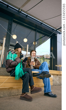 Friends relaxing with takeaway coffee outside neighborhood cafe in winter. Friends relaxing with takeaway coffee outside neighborhood cafe in winter. 133855593