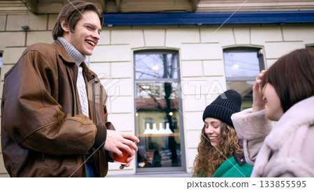 Friends laughing and enjoying hot coffee together outside city cafe in winter 133855595