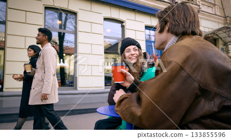 Friends enjoying warm coffee and casual conversation outside city cafe in winter. Friends enjoying warm coffee and casual conversation outside city cafe in winter. 133855596