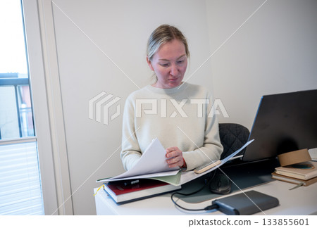 Woman reviewing documents while working at home office desk 133855601
