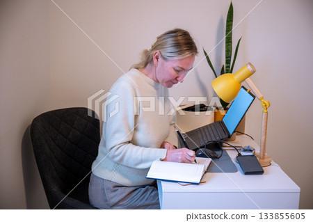 Woman writing in notebook while working at home office desk 133855605