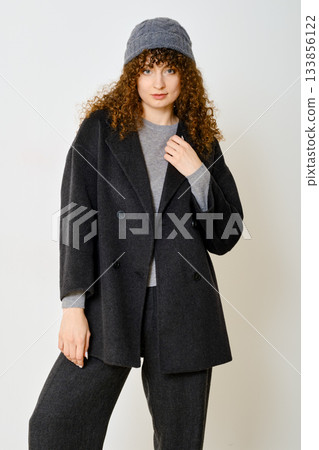 Stylish woman wearing a black jacket and grey outfit poses confidently in a modern setting 133856122