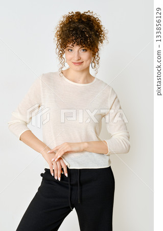 Young woman poses in light sweater and black sweatpants against neutral background Young woman poses in light sweater and black sweatpants against neutral background 133856129