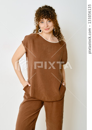 Stylish woman poses in a brown outfit against a plain background in a relaxed setting Stylish woman poses in a brown outfit against a plain background in a relaxed setting 133856135