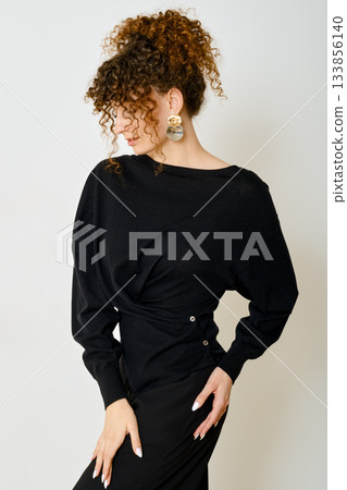 Curly haired model poses elegantly in black outfit highlighting unique style and accessories 133856140