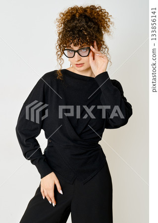 Stylish woman wearing black outfit poses with confidence against simple background Stylish woman wearing black outfit poses with confidence against simple background 133856141