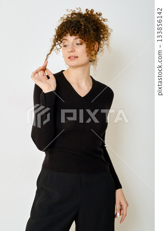 Woman with curly hair in a black sweater poses thoughtfully against a plain background Woman with curly hair in a black sweater poses thoughtfully against a plain background 133856142