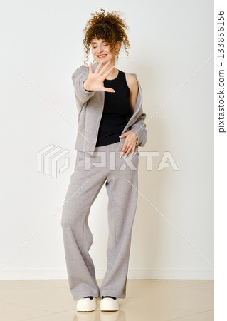 Young woman in casual grey outfit poses playfully in an indoor setting with a bright background Young woman in casual grey outfit poses playfully in an indoor setting with a bright background 133856156