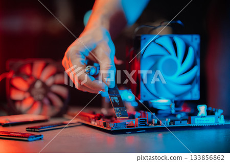 system administrator installing SSD into motherboard, assembling PC of different accessories or components, close-up view of hands, computer repair and maintenance concept 133856862