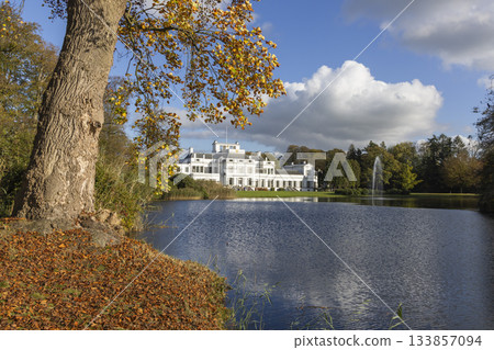 Soestdijk Palace reflected in the calm waters of the Baarn lake on a sunny autumn day with colorful leaves 133857094