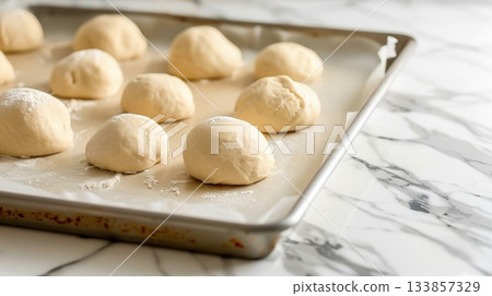 Pieces of raw dough being placed on a baking sheet on a baking tray 133857329
