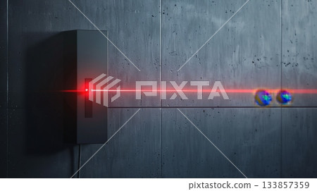 A laser beam projects from a black device onto a concrete wall. The beam is red and interacts with two colorful spheres in the foreground. A laser beam projects from a black device onto a concrete wall. The beam is red and interacts with two colorful spheres in the foreground. 133857359