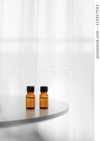 Essential oil bottles lined up on a white round table by the window, vertical composition, copy space 133857583