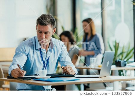 Young Professional Preparing for Meeting in Modern Office Cafe with Laptop and Notes Young Professional Preparing for Meeting in Modern Office Cafe with Laptop and Notes 133857906