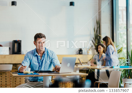 Young Professional Preparing for Meeting in Modern Office Cafe with Laptop and Notes Young Professional Preparing for Meeting in Modern Office Cafe with Laptop and Notes 133857907