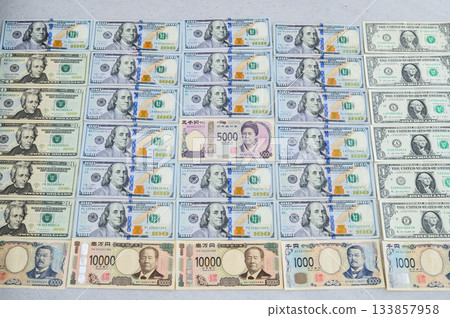 一張100美元鈔票、一張10000日元鈔票、一張5000日元鈔票，周圍是一群男人，其中一位是女性領導者，鈔票略微向上傾斜。 133857958