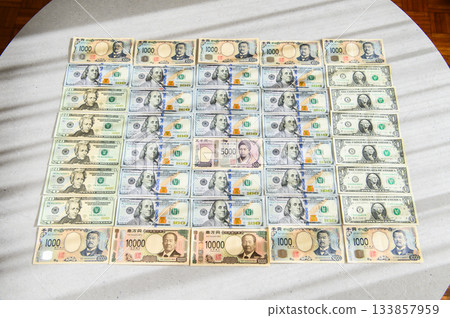 一張100美元鈔票、一張10000日元鈔票、一張5000日元鈔票，周圍是一群男性，其中一位是女性領導者，畫面略寬。 133857959