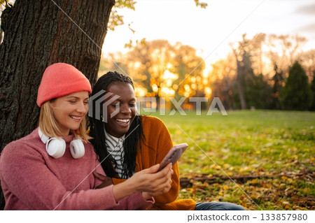 Diverse friends enjoying autumn park looking at smartphone Diverse friends enjoying autumn park looking at smartphone 133857980