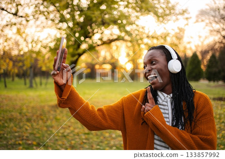 Happy young adult woman enjoying video call in park 133857992