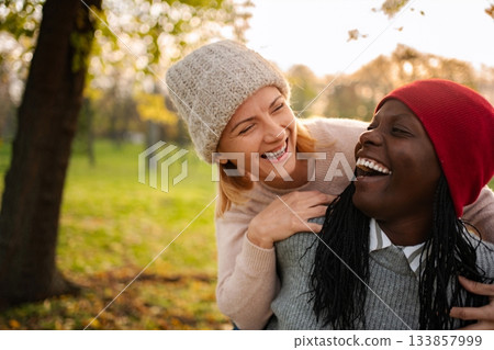 Diverse women friends laughing together enjoying autumn park Diverse women friends laughing together enjoying autumn park 133857999