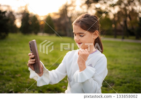 Young girl having video call with friends family in park Young girl having video call with friends family in park 133858002