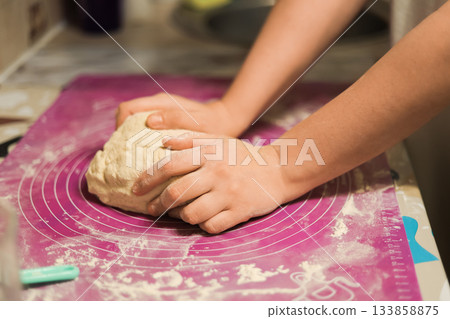 A pair of hands vigorously kneading a mound of fresh dough on a purple silicone baking mat covered in a light dusting of flour. High quality photo 133858875