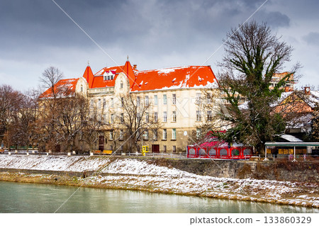 uzhhorod, ukraine - 15 feb 2009: uzh river in the old city in winter. cityscape with snow on the embankment. european urban landscape with school building. dramatic weather with cloudy sky 133860329