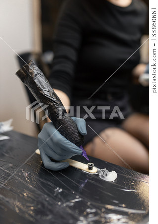 tattoo artist in gloves holding a tattoo machine during a session, preparing tools in a professional studio environment. tattoo artist in gloves holding a tattoo machine during a session, preparing tools in a professional studio environment. 133860661