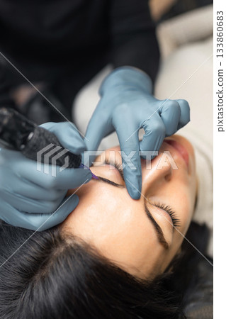Close up of a cosmetologist performing eyebrow microblading on a female client. Professional beauty procedure, sterile tools, precision work and eyebrow shaping in a modern beauty studio. Close up of a cosmetologist performing eyebrow microblading on a female client. Professional beauty procedure, sterile tools, precision work and eyebrow shaping in a modern beauty studio. 133860683