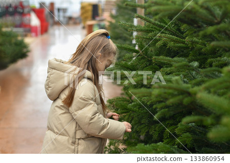 Small girl chooses a Christmas tree in the market. 133860954